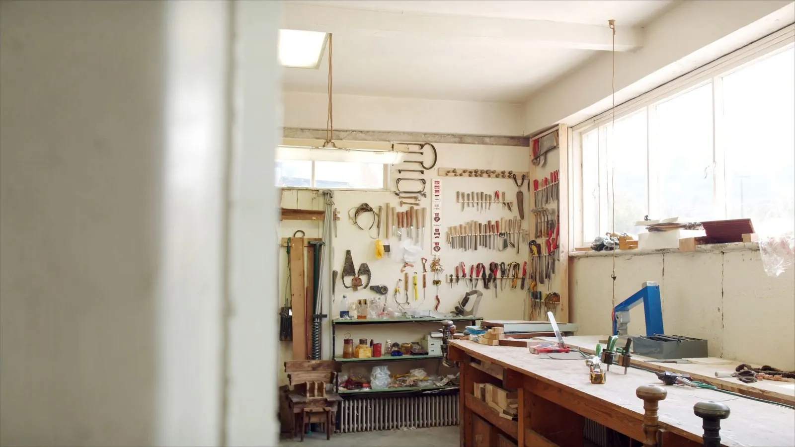 A bright joinery workshop with tools hung in order on the wall and a clear bench under high windows