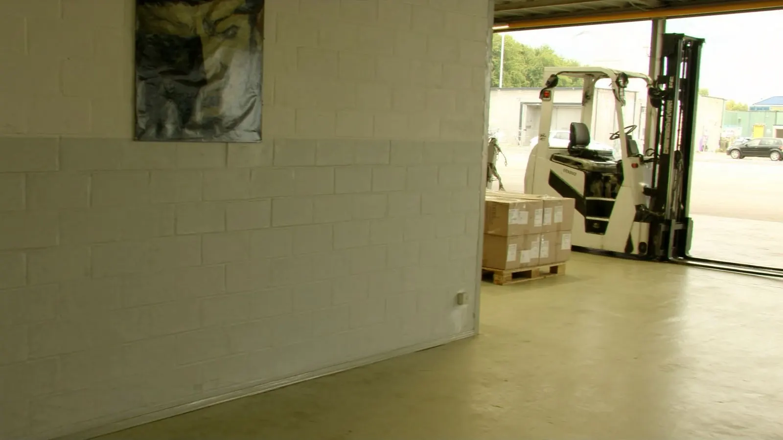 A fork lift truck and a pallet of boxed stock on the clean floor of a bright light industrial unit, the shutter open to daylight